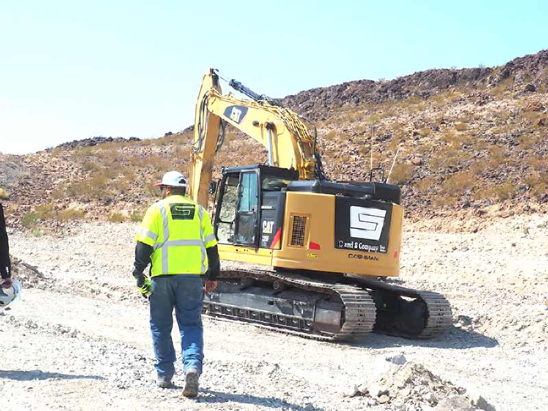 A worker in hi-vis beside a branded C and S excavator