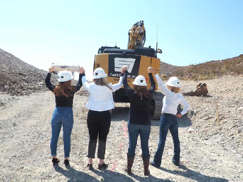 C and S crew members raising their hard hats in front of a company excavator